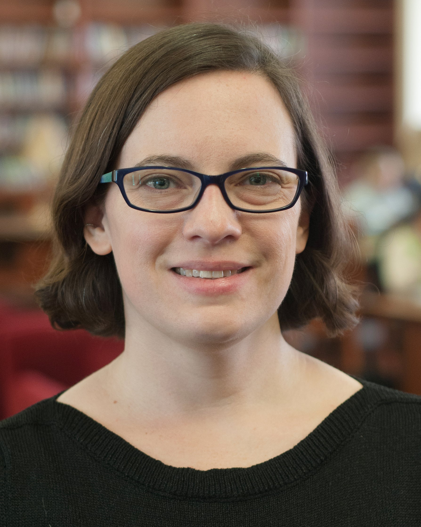 Photo of Liz Petrick, a female with chin length hair and rectangular glasses, in front of a bookcase